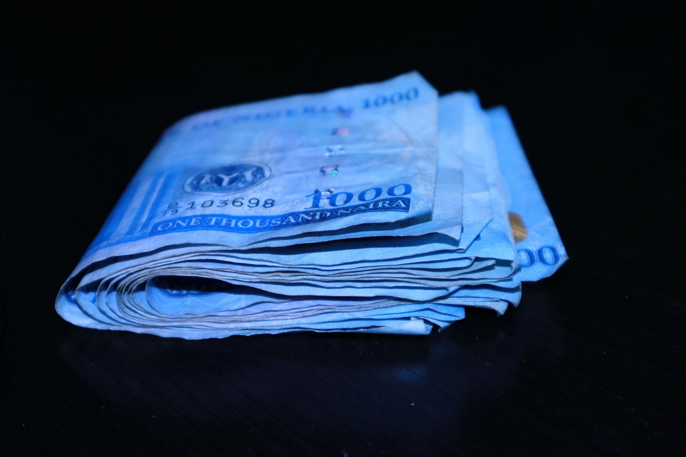 A folded stack of one-thousand-naira notes on a dark table
